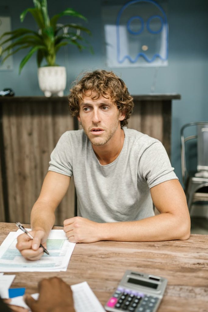 Young man focused on paperwork with a calculator and documents at a wooden desk in a modern office.